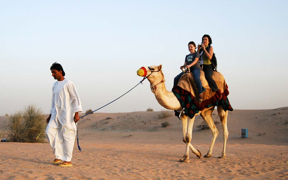 Tourists enjoying traditional camel riding during Dubai desert safari adventure