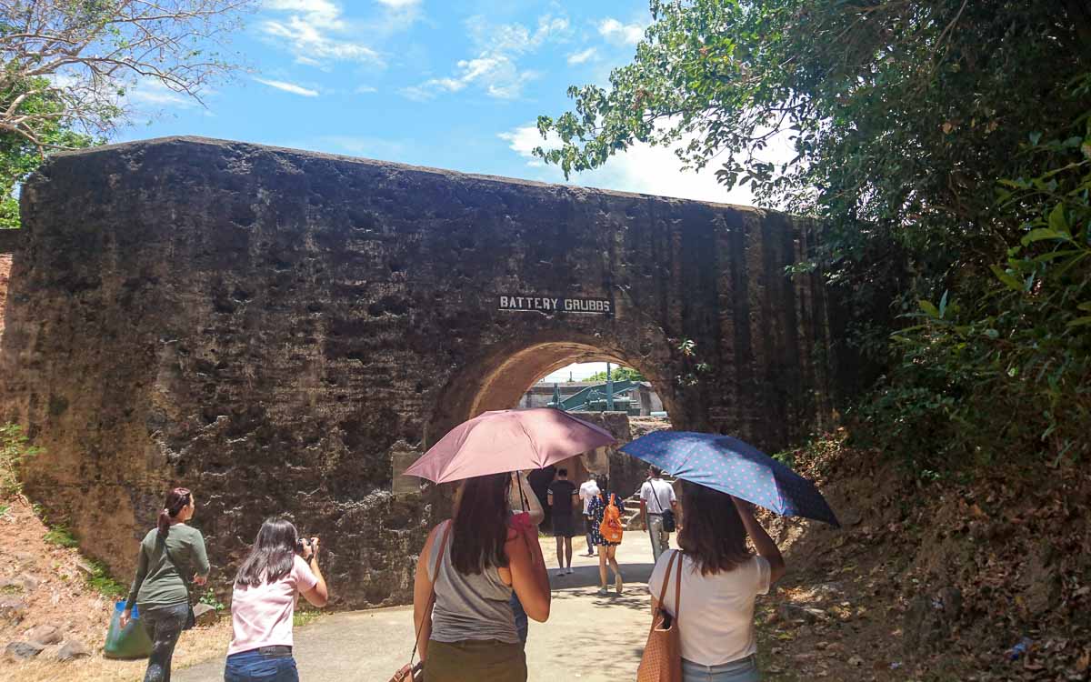 a group of people passing under a stone entrance at Battery Grubbs in Corregidor 