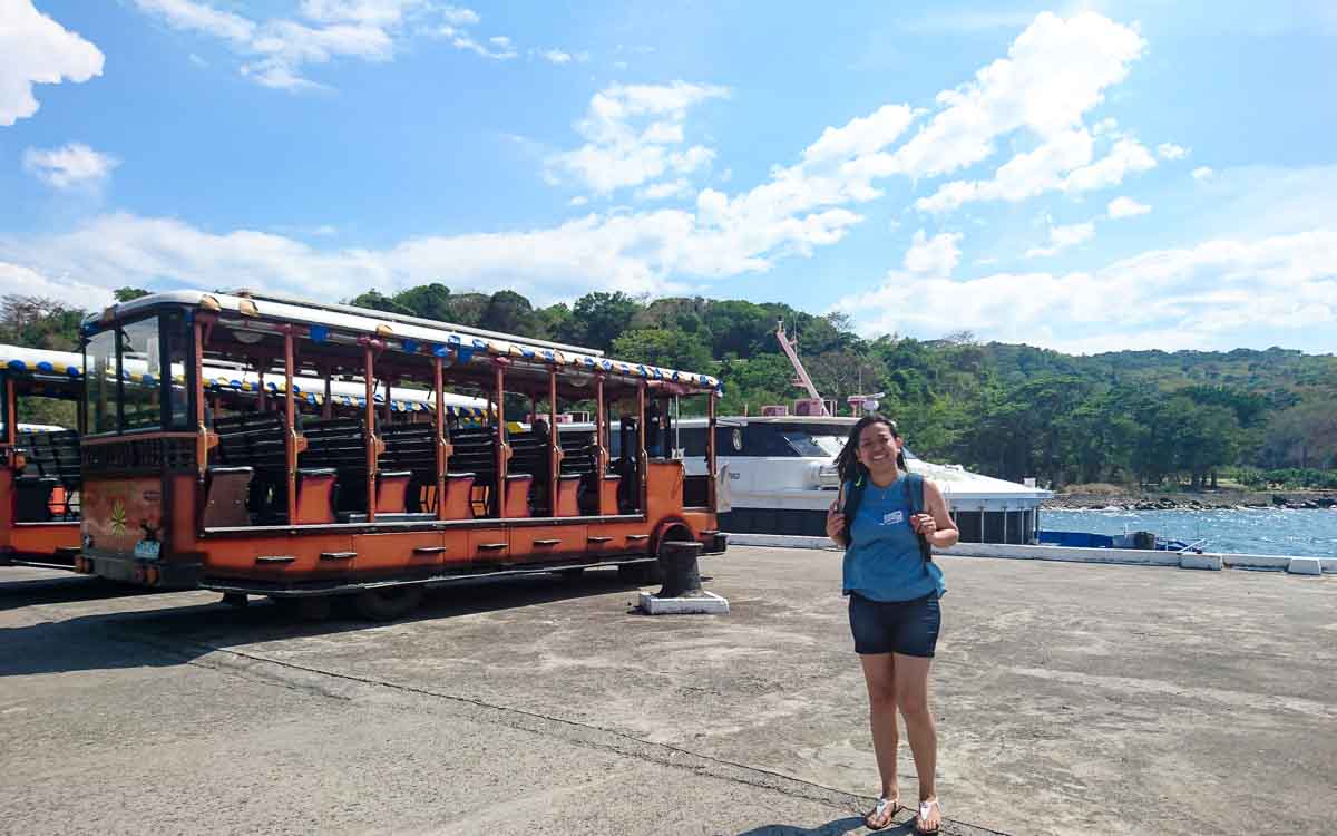 a woman in a blue skirt standing next to a tram vehicle at the port of Corregidor