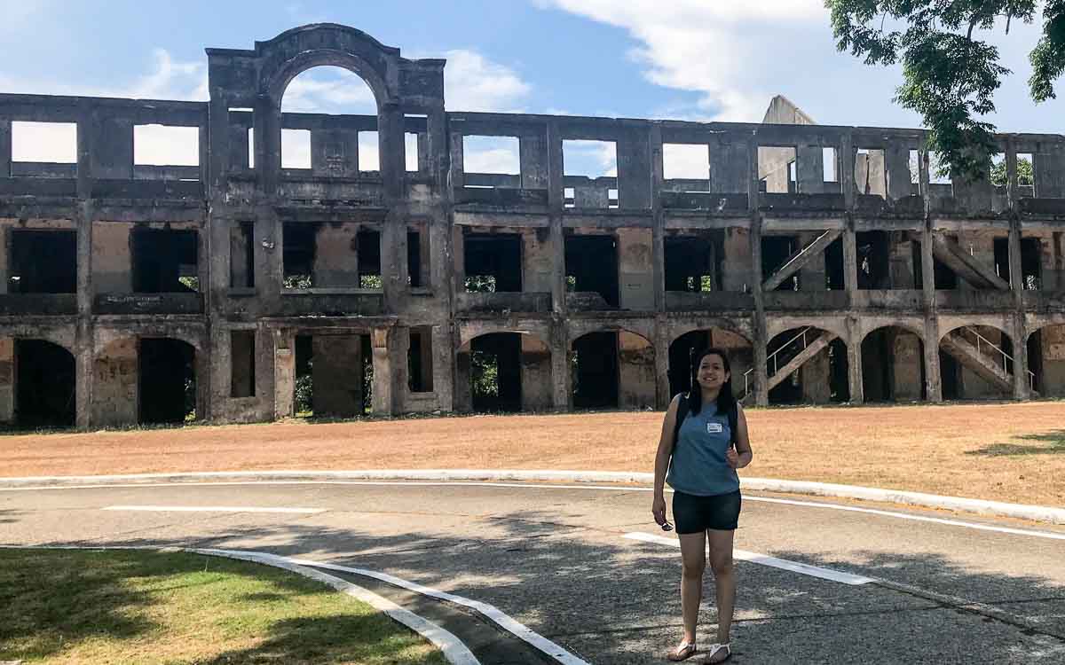 a woman standing in front of the ruins of Mile Long Barracks at Corregidor