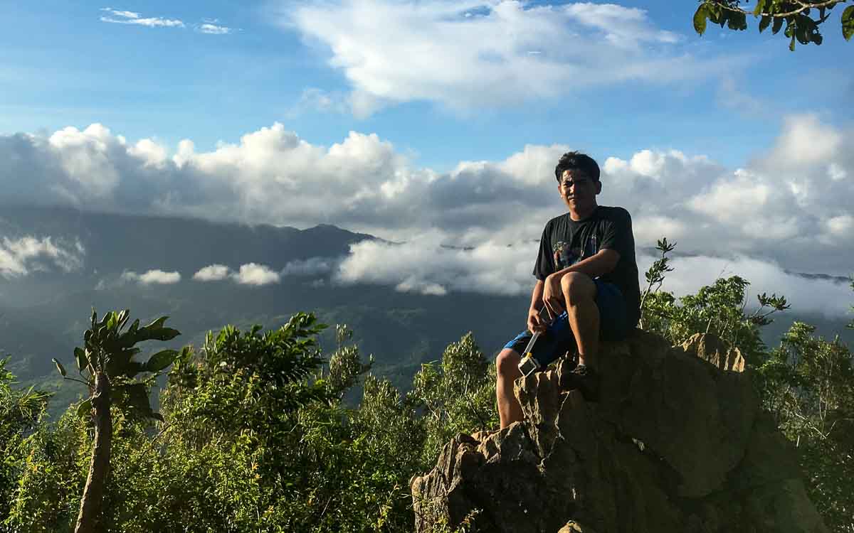 A man wearing a black shirt is sitting on the rock at the summit of Mount Daraitan