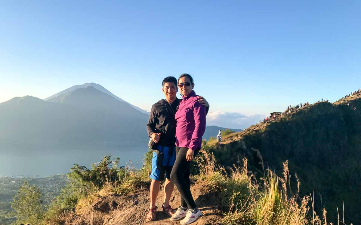 Happy couple portrait at Mount Batur volcano summit after successful sunrise hike in Bali