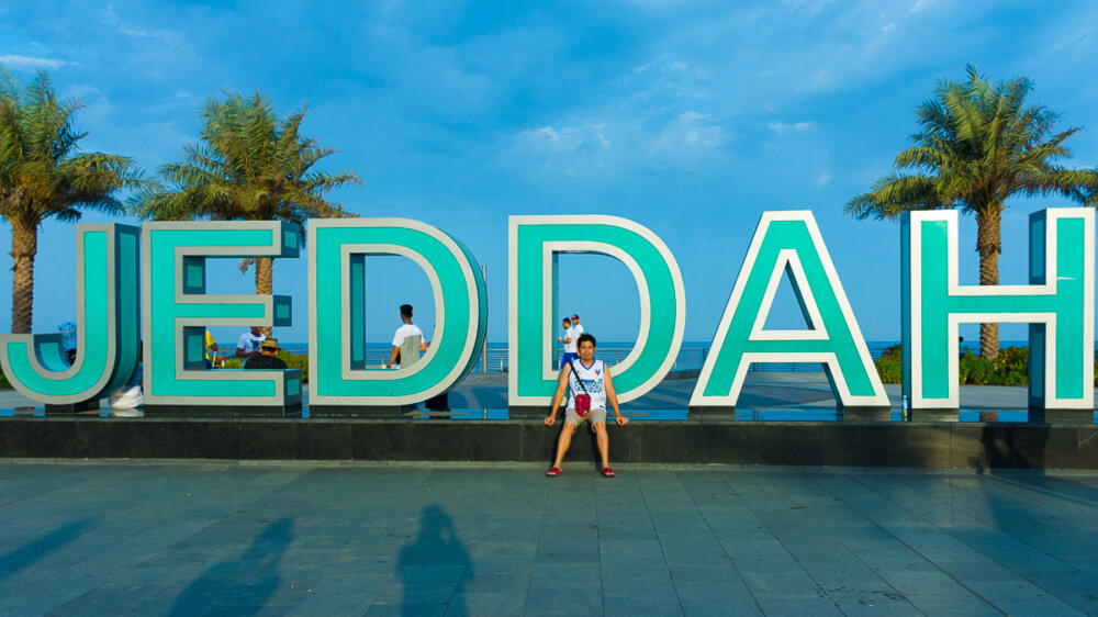 a man sitting infront of Jeddah sign at Corniche Waterfront